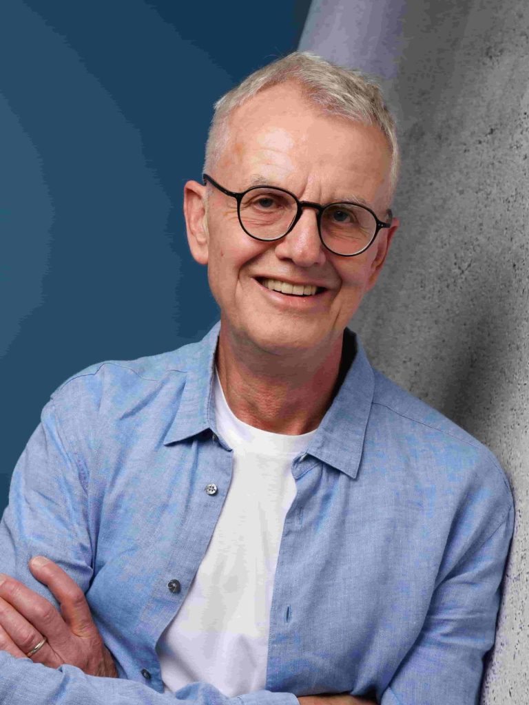 Detlef Flintz, Politik-Berater Lachend mit verschränkten Armen in hellblauen Hemd an Wand lehnend